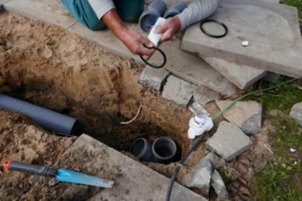 Plumber repairing underground pipe in an excavated trench, Aledo, TX